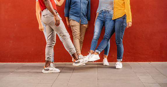 Group of young men and women in front of red wall making foot bump.