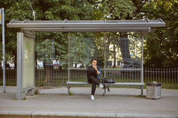 istock Young man with laptop on bus stop. 1272493855