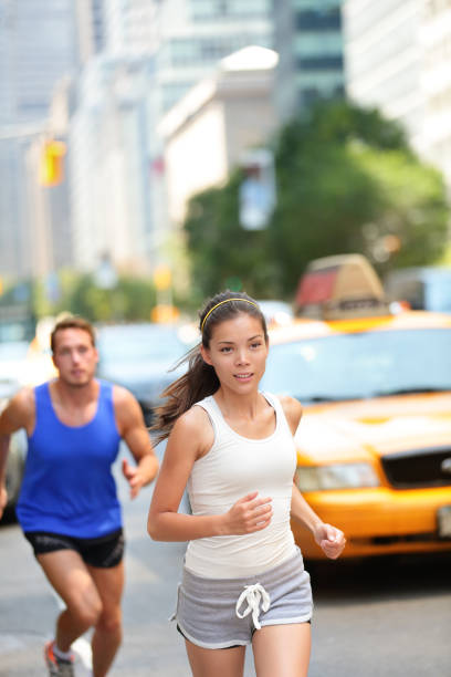Running workout in New York City - Runners couple Running workout in New York City. Urban runners people jogging in busy street in New York NYC. Young adults asian caucasian jogging in traffic on Manhattan during summer training for Marathon. new york marathon photos stock pictures, royalty-free photos & images