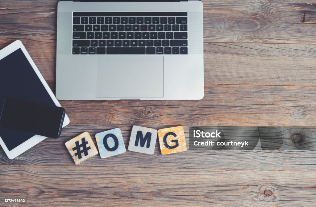 OMG, Oh My God acronym. Laptop, digital tablet and mobile phone with a hashtag and the letters OMG beside them. OMG, Oh My God acronym. Laptop, digital tablet and mobile phone with a hashtag and the letters OMG beside them. They are on a wooden background with copy space. Acronym Stock Photo