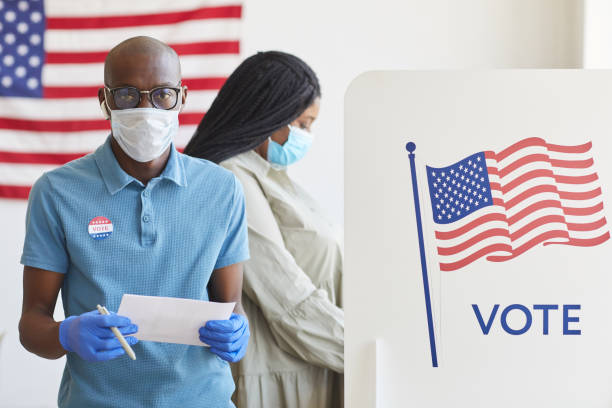 African-American Man Voting Post Pandemic Waist up portrait of African-American man standing by voting booth decorated with USA flag and looking at camera on post-pandemic election day, copy space ballot measure stock pictures, royalty-free photos & images