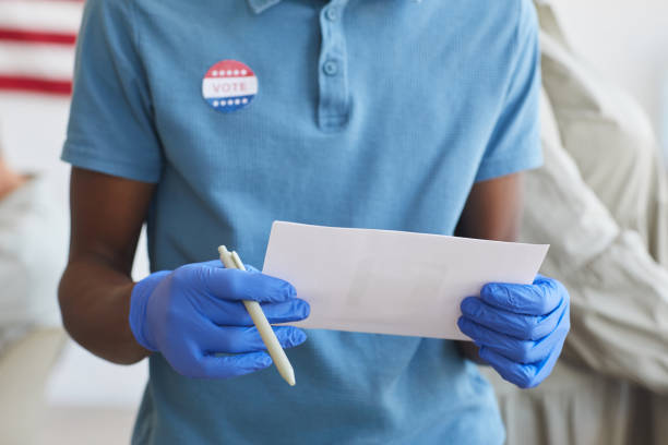African-American Man Holding Voting Ballot Cropped portrait of unrecognizable African-American man holding ballot and standing by voting booth on post-pandemic election day, copy space ballot measure stock pictures, royalty-free photos & images