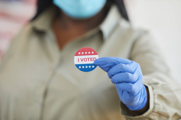 I VOTED in Pandemic Close up of unrecognizable African-American woman holding I VOTED sticker while standing at polling station on post-pandemic election day, copy space ballot measure stock pictures, royalty-free photos & images