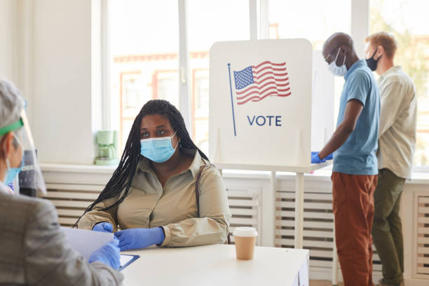 Covid Safety at Polling Station Multi-ethnic group of people wearing masks voting at polling station on post-pandemic election day, copy space ballot measure stock pictures, royalty-free photos & images