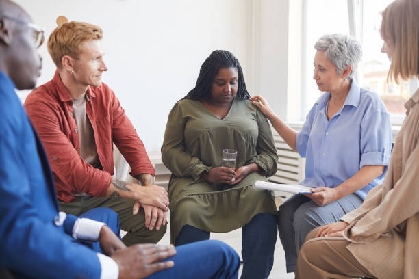 African Woman in Group Therapy Session Portrait of young African-American woman sharing struggles during support group meeting with people siting in circle and comforting her group therapy photos stock pictures, royalty-free photos & images