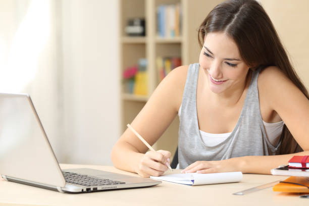istock Happy student reading on laptop taking notes at home 1272497546