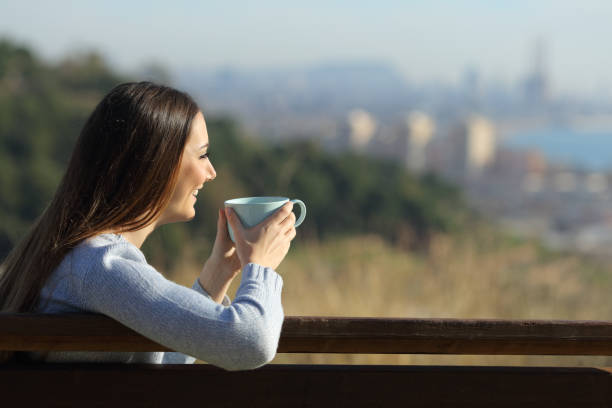 istock Happy woman holding a coffee cup sitting on a park 1272497572