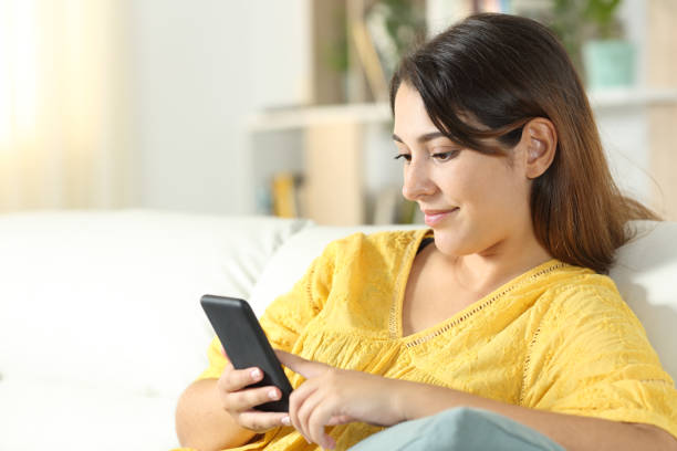 istock Girl in yellow using mobile phone on a sofa at home 1272498291