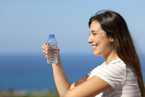 Happy woman holds bottled water in a hotel balcony