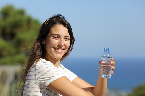 Happy woman holding a bottle of water looks at you