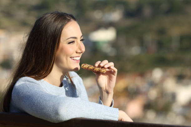 istock Happy woman eating cereal bar on a park bench 1272498475