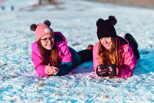 Two Female Teenagers Lying Down On Mountain Snow