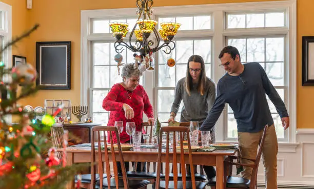 Photo of Young couple and senior woman, a mother, laying the table for the Christmas holiday family dinner.