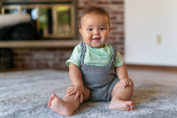 istock Laughing baby sitting on floor at home 1272506182