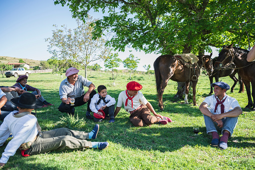 Gaucho boys, teenagers, and adults relaxing and talking under shade tree on estancia near Cordoba in Argentina.