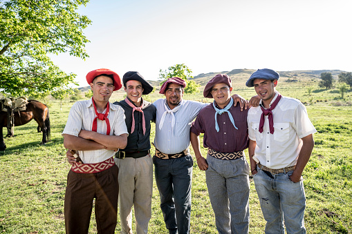 Close-up of relaxed young gaucho teenagers and adult standing together with arms around each other and smiling at camera.