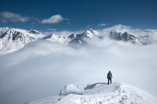 Man standing on the top of a snowcapped mountain peak with amazing view.