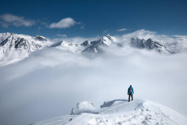 Mountain Hiking Man standing on the top of a snowcapped mountain peak with amazing view. wonderlust stock pictures, royalty-free photos & images