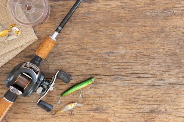 Fishing rod cork handle with reel and plastic fish bait. Fishing rod cork handle with reel and plastic fish bait lures have sharp metal hoop pace on old wood table for background, Vintage wood and fishing equipment, Holiday travel to fishing are hobbies. fishing tackle stock pictures, royalty-free photos & images