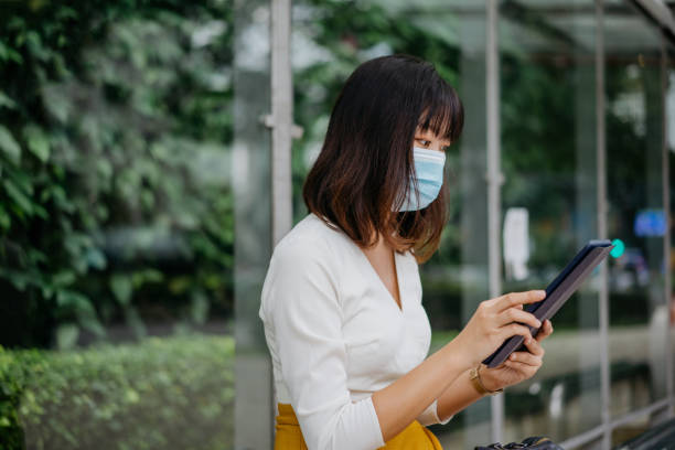 istock Young asian businesswoman with face mask using digital tablet at bus stop while waiting for public transport 1272517565