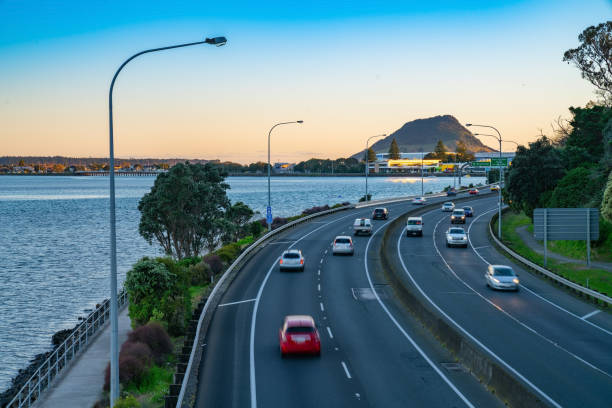 Cars in long exposure  blurred in motion travelling along Takitimu Drive, Tauranga. Cars in long exposure  blurred in motion travelling along Takitimu Drive with landmark Mount Maunganui in distance at sunrise mount maunganui stock pictures, royalty-free photos & images