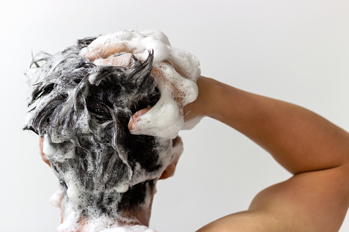 Un hombre se lava la cabeza con champú sobre fondo blanco, vista trasera photo