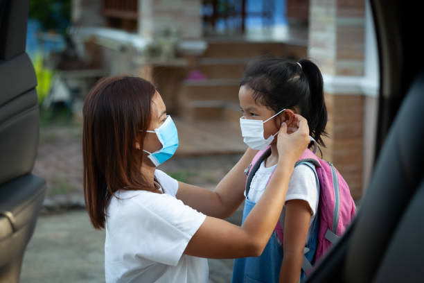 asian mother help her daughter wearing protection mask to protect the coronavirus covid-19 outbreak situation before go to school. get ready to school concept. - illness mask pollution car imagens e fotografias de stock