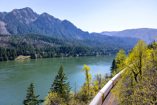 Landscape with a freight train on a railroad running along the banks of the Columbia River with a mountain range and trees in Columbia River Gorge National Reserve - dream to visit for every tourist