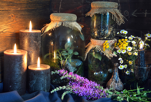 Black candles and magic bottles with plants and herbs on witch table.  Esoteric, gothic and occult background, Halloween mystic concept.