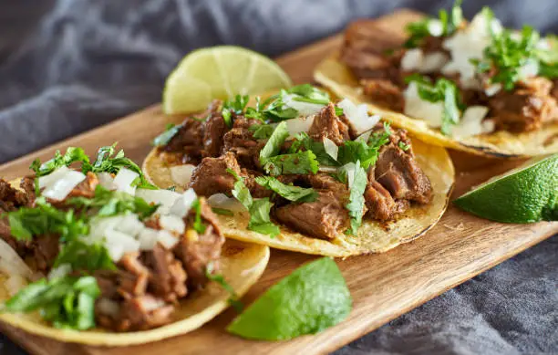 three carne asada mexican street tacos in corn tortilla with lime close up