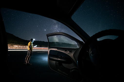 Milky way adventures. Sunday night adventures. A middle-aged handsome man changing his car tire in a deserted place somewhere in the wild. Urgency measures.