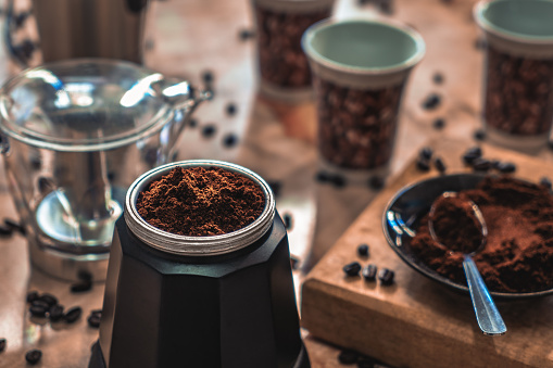 Disassembled coffee maker on a table with ground coffee, surrounded by coffee stuff