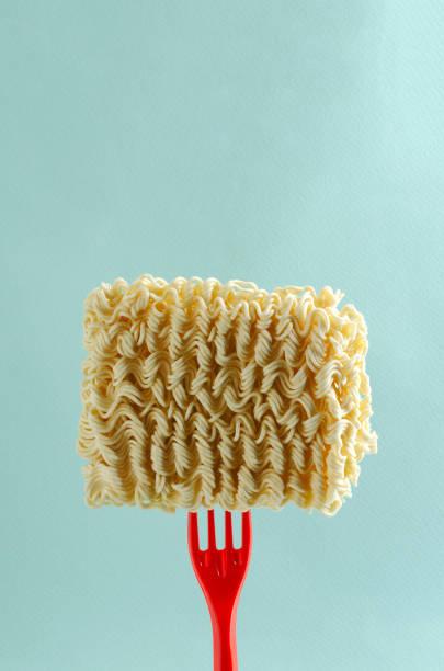 istock Red plastic fork and dry noodles on it against blue background 1272539710
