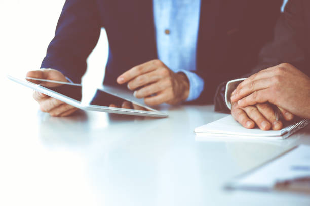 istock Two unknown businessmen or partners using tablet pc and discussing questions at meeting in modern office, close-up of hands. Group of managers at negotiation or brainstorm. Teamwork, partnership and business concept 1272541687