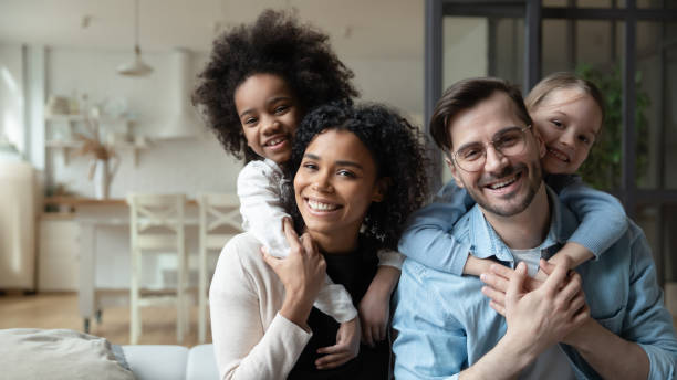 Happy multiracial couple enjoying sweet family moment with children. Portrait of happy multiracial couple enjoying sweet family moment with adorable little mixed raced daughters at home. Smiling cute small stepsisters cuddling cheerful parents, looking at camera. social services photos stock pictures, royalty-free photos & images