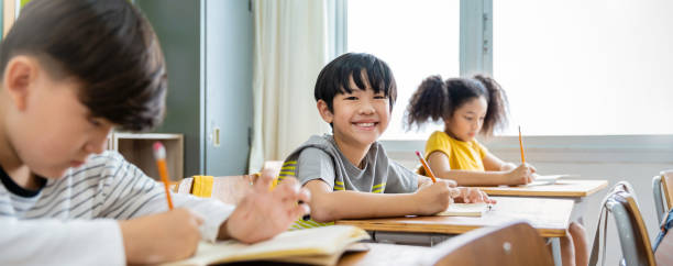 小学校の教室の机に書いている小さな生徒の肖像画。小学校でテストをしている学生のボイル。教室でメモを書く子供たち。教育知識バナー - elementary student little boys classroom child ストックフォトと画像