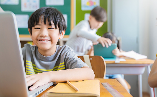 Retrato de niño asiático usando computadora para aprender lecciones en la escuela primaria. Estudiante que estudia en primaria. Niños con aparatos en el aula. Conocimientos educativos, concepto de red de Internet tecnológica photo