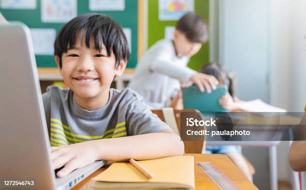 Portrait Of Asian Little Boy Using Computer To Learn Lessons In Elementary School Student Boy Studying In Primary Children With Gadgets In Classroom Education Knowledge Technology Internet Network Concept Stock Photo - Download Image Now