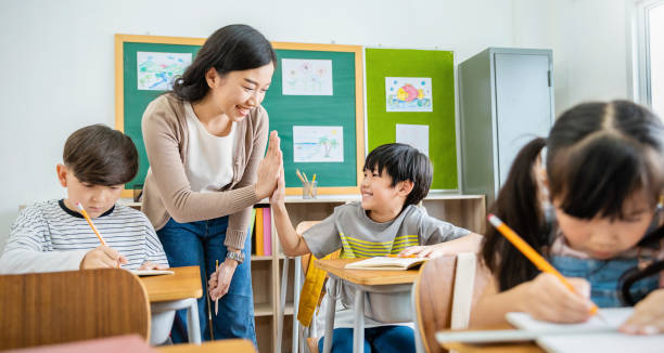 小学校の教室で先生と一緒に5人の生徒の男の子こんにちは。小学校で勉強している学生の男の子。教室でメモを書く子供たち。教育知識、成功したチームワークコンセプト - 教授 ストックフォトと画像