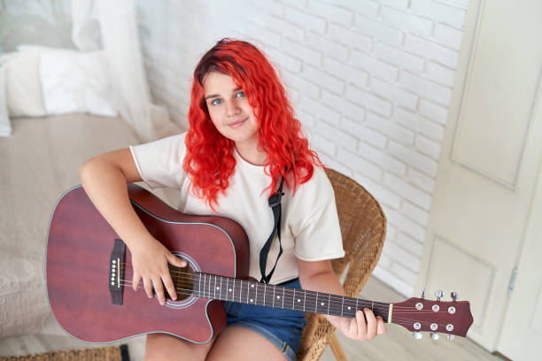 teenage girl of 12 years old holding a guitar and smiling - 12 13 years fotos imagens e fotografias de stock