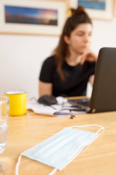 istock Female student taking notes and e-learning with a laptop working at home office, social distancing - quarantine. New normal, illness prevention. Defocused, focus on protective face mask. 1272551537