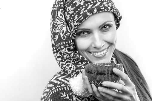 Cheerful young woman in christmas outfit knitted hat and sweater holding hot drink isolated over white