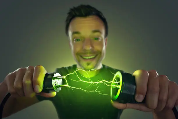 Smiling man holding a power plug and socket in his hands. Green electrical lightning between the plug and socket. Concept for green energy.