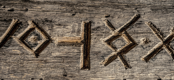 Ancient Scandinavian runes carved into the surface of an old dry wooden board. Vintage background and texture