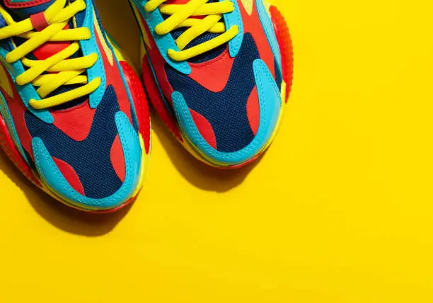 Photo of Multicolor sport shoes on yellow background with shadows