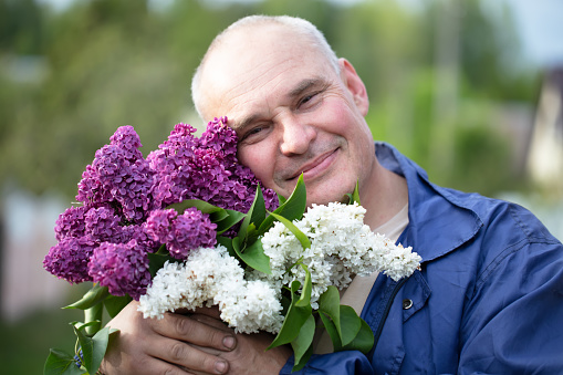 Elderly man with a bouquet of flowers. Brutal gray-haired man with a beautiful lilac.