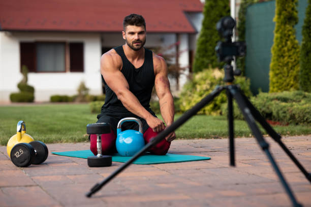 istock Male athlete sitting on exercise mat and making vlog at backyard. 1272566458