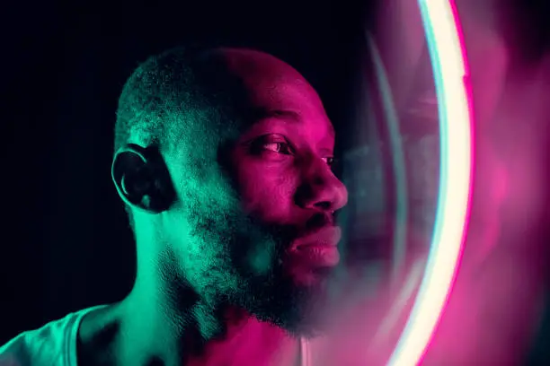 Photo of Cinematic portrait of handsome young man in neon lighted room, stylish musician