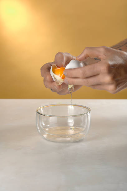 istock cracking a white egg above a glass bowl on white marble table with yellow background 1272568276