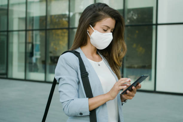 istock Businesswoman with protective face mask using smart phone outdoors 1272570372